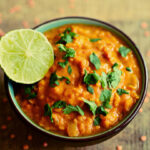 A bowl of red lentil curry (masoor dal) garnished with coriander and served with a slice of lime