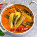 A bowl of toor dal sambar with okra, tomato, and spices in a tangy tamarind broth